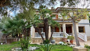 Una casa de dos pisos con un balcón, rodeada de plantas y un camino de piedra.