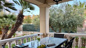 Un patio techado al aire libre con una mesa para dos personas, que incluye una computadora portátil, un vaso de agua, una botella de agua y un bol de uvas.
