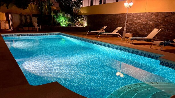 Una piscina con un diseño geométrico de azulejos, rodeada de sillas de descanso y un muro de piedra.
