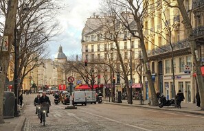 Un carrer empedrat amb edificis històrics, una estàtua i un tram.