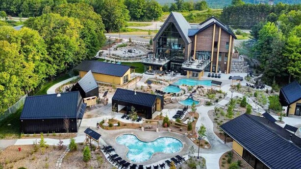 Een resort met een groot zwembad, terras en een modern gebouw met glazen gevel.