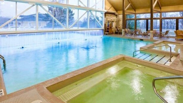 Ein Innenpool mit großen Glaswänden, ein separater Whirlpoolbereich und Liegestühle am Rand.