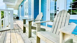 Terraza de madera con sillas Adirondack y una mesa, con vista a una piscina.