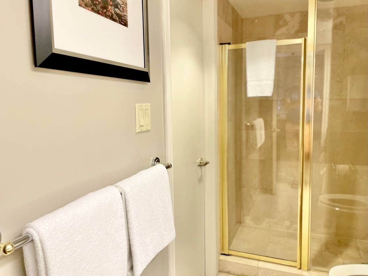 A bathroom with a glass shower enclosure, a white towel hanging on a towel rack, and a framed picture on the wall.