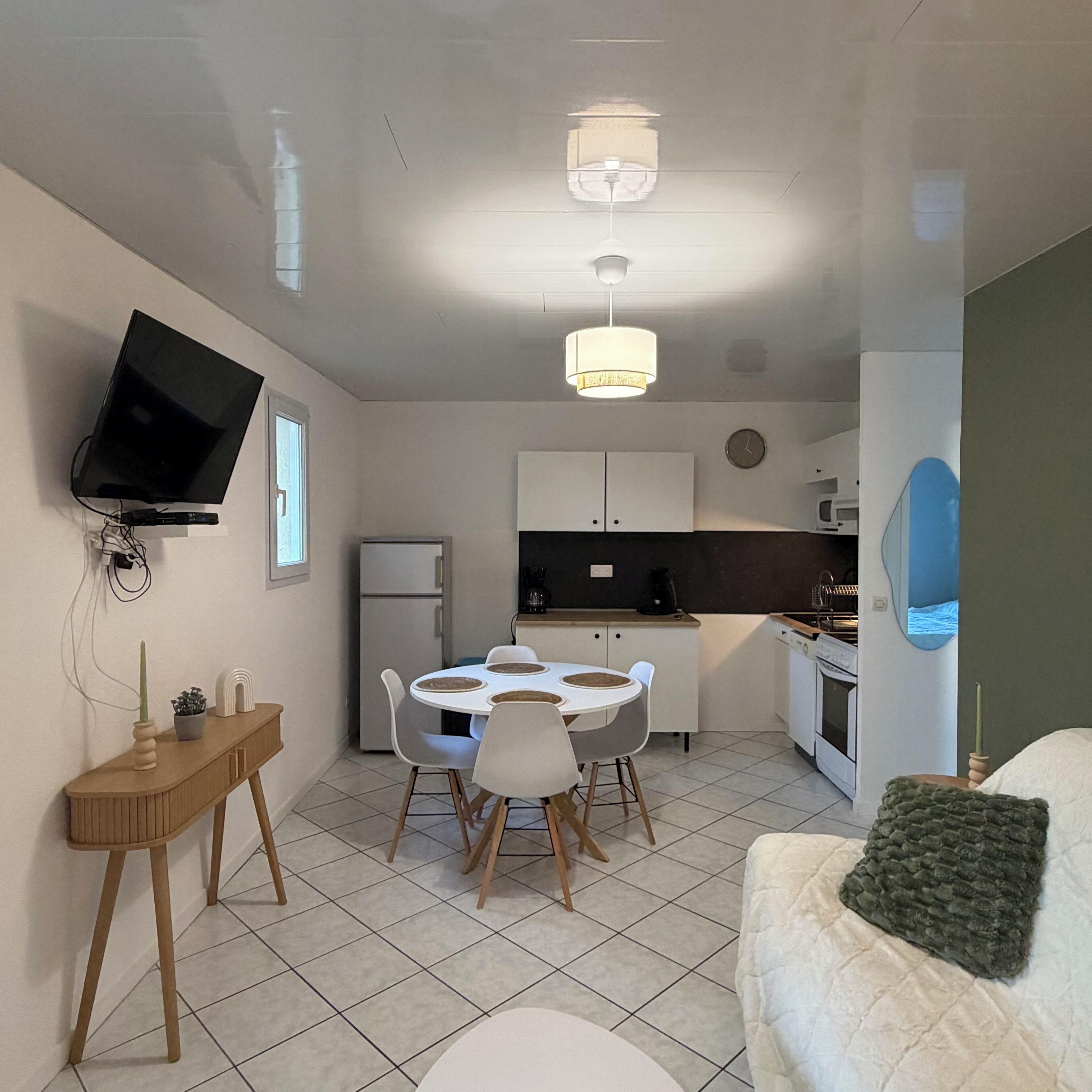 A compact living space with a dining area, kitchenette, and a TV mounted on the wall.