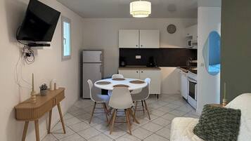 A compact living space with a dining area, kitchenette, and a TV mounted on the wall.