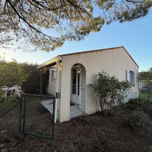 Une petite maison de plain-pied, avec un toit recouvert de tuiles, une porte d’entrée et un petit porche.