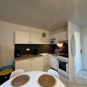 Une cuisine compacte avec des meubles blancs, un four à micro-ondes, une cuisinière et un évier. On y trouve une table ronde avec deux sets de table et une chaise.