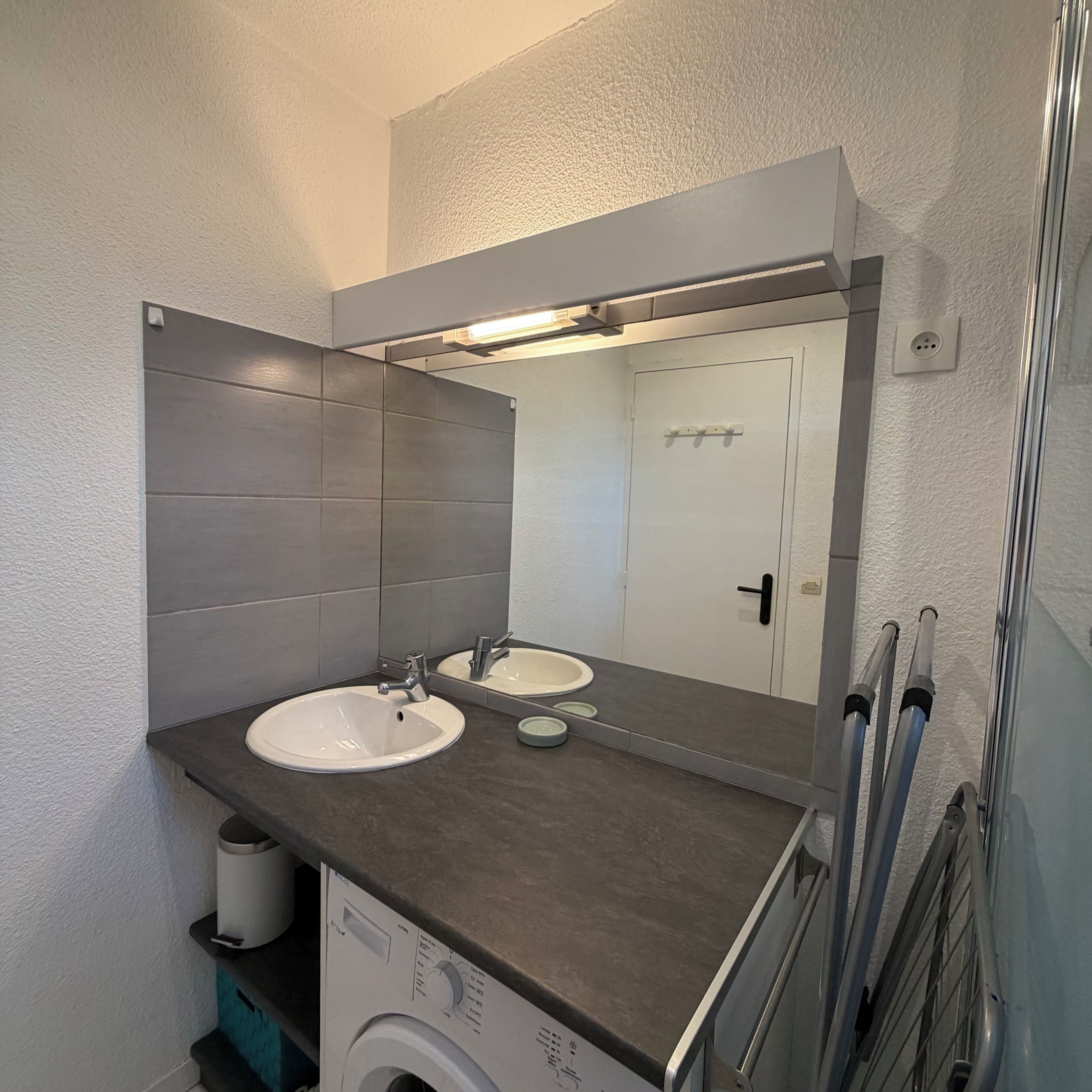 Uma casa de banho moderna com duas pias, um espelho grande e uma máquina de lavar integrada.