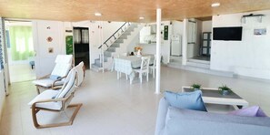 Ein modernes Wohnzimmer mit Sofa, Sesseln, einem Esstisch und einer Treppe, die in eine Küche führt.
