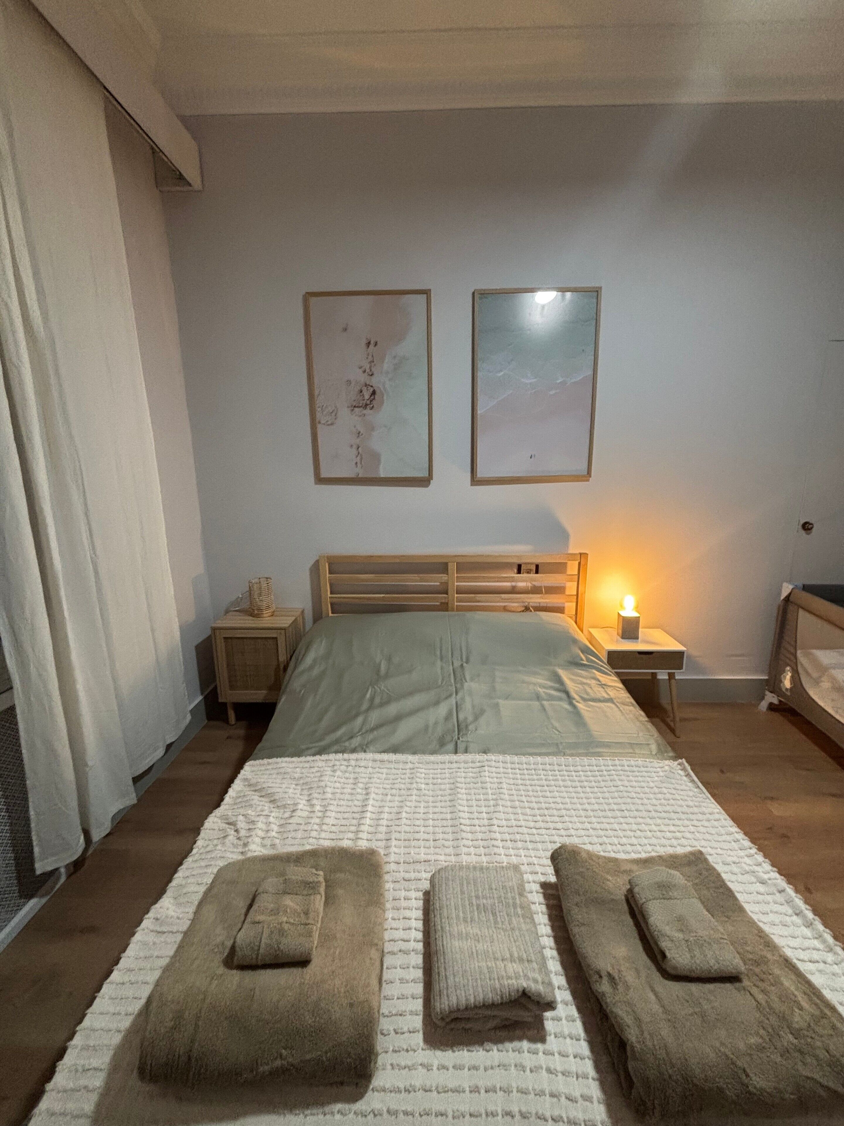 Un dormitorio con cama, dos mesitas de noche, una lámpara y una ventana con cortinas.