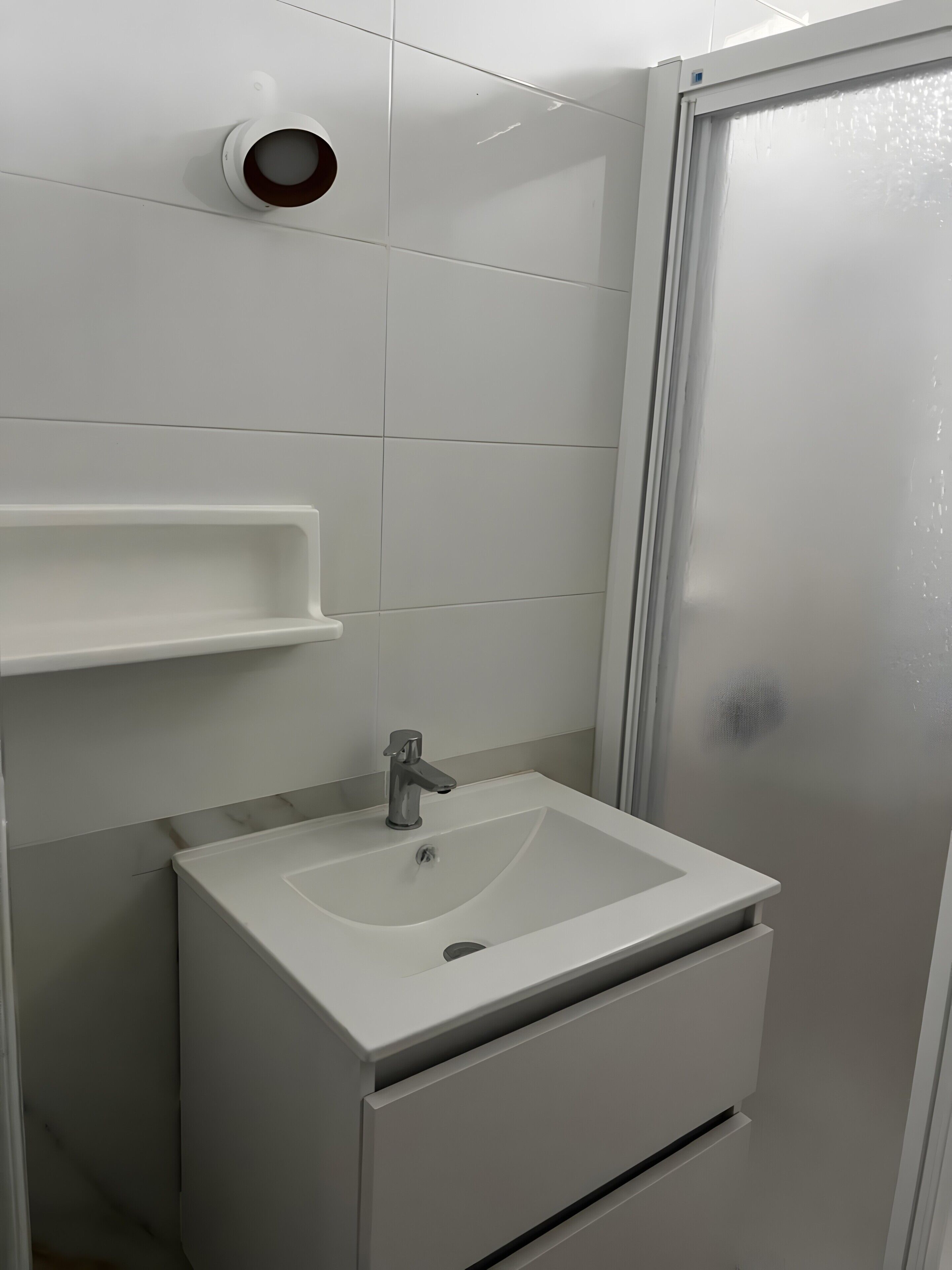 Une salle de bain avec un lavabo blanc, un miroir et un espace douche.