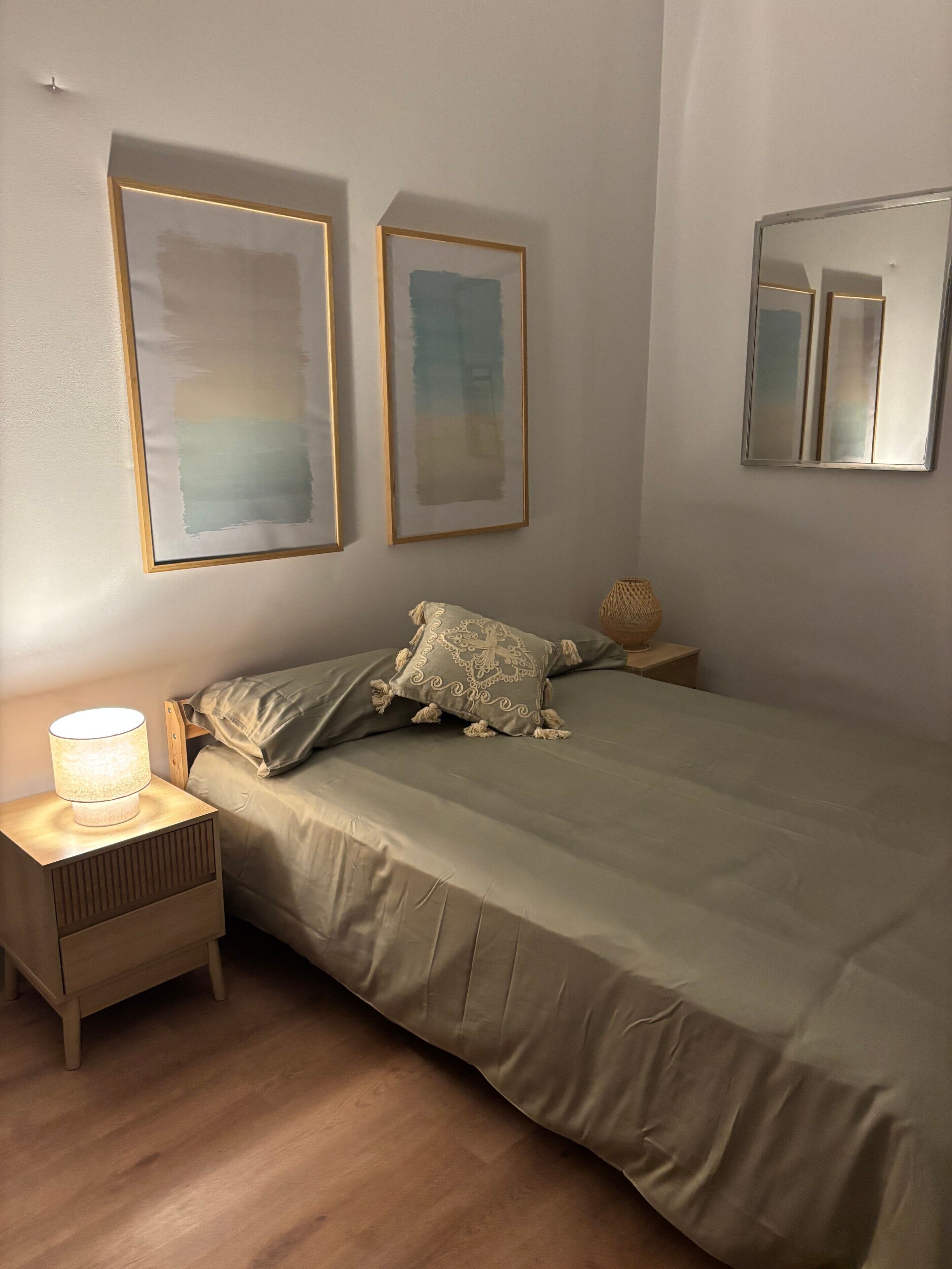 Een slaapkamer met een bed, een nachtkastje, een lamp en twee ingelijste kunstwerken aan de muur.