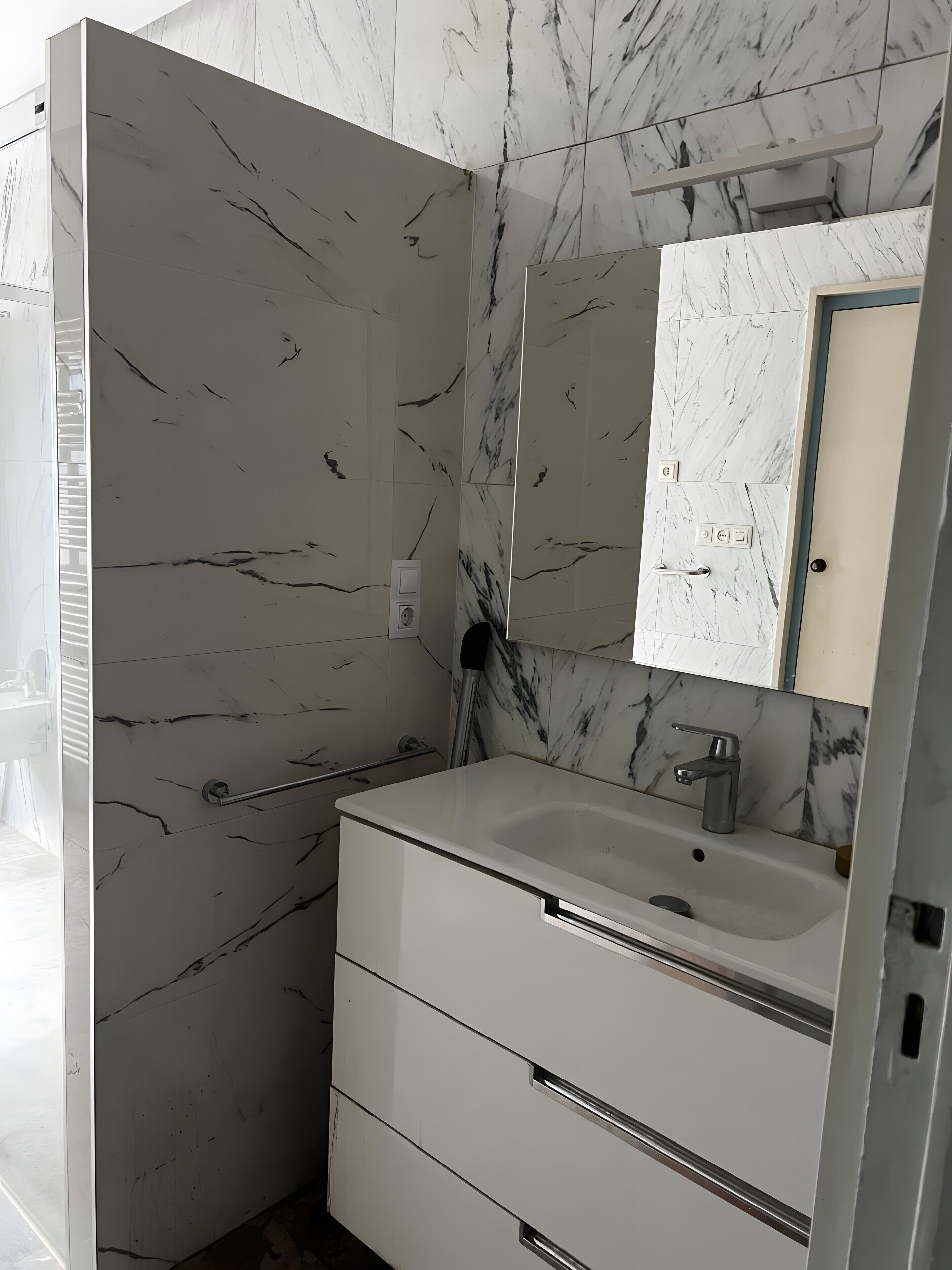 Un baño con paredes de mármol, un lavabo con espejo y un perchero para toallas.