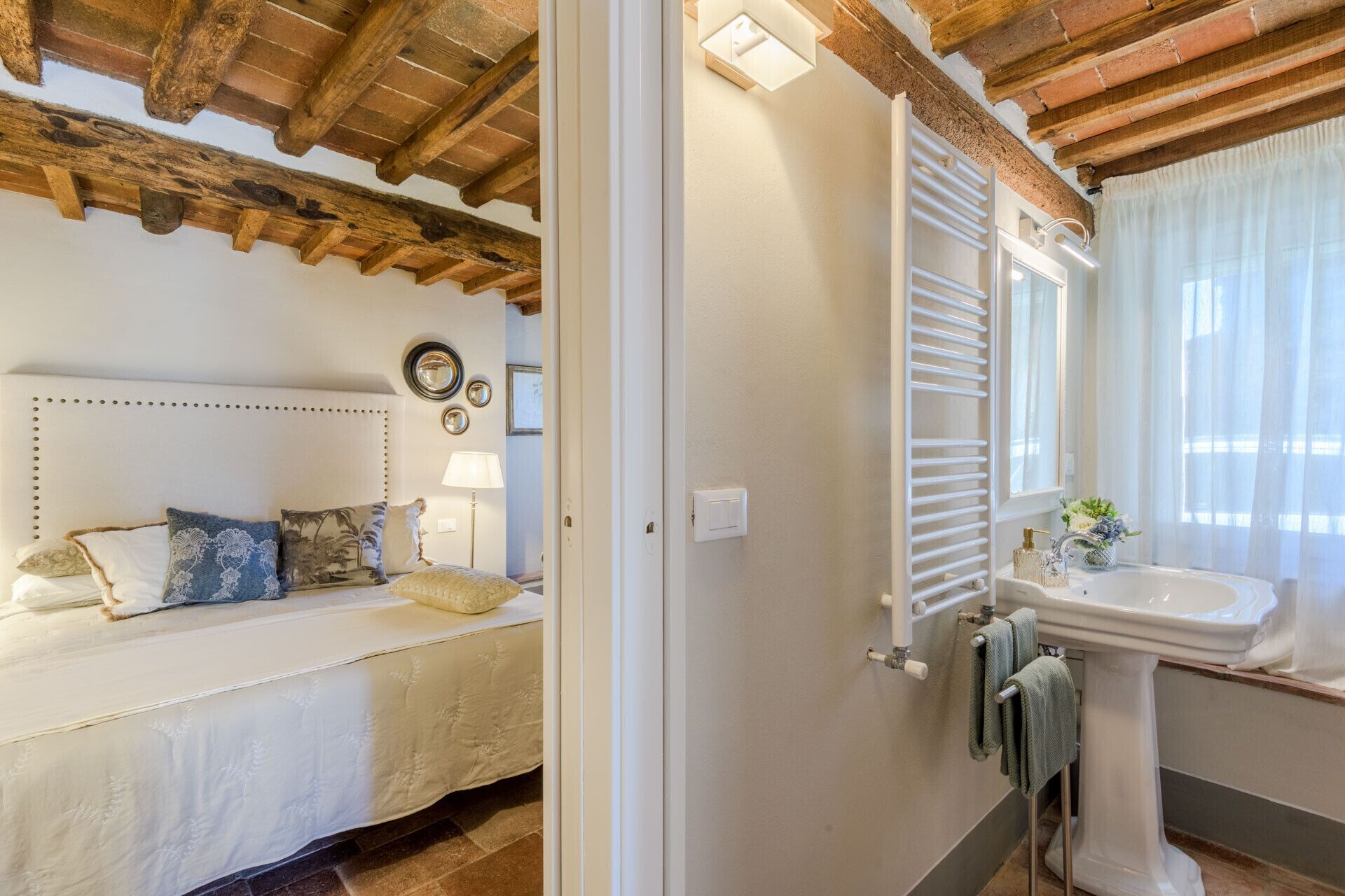 Een slaapkamer met een houten plafond, een bed met decoratieve kussens, een bedlamp en een spiegel aan de muur.