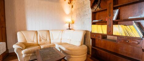 Una sala de estar acogedora con un sofá de cuero blanco, una mesa de centro de madera y una estantería con libros y objetos decorativos.
