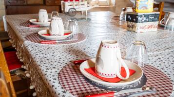 Una mesa de comedor dispuesta con platos, vasos y cubiertos, con un mantel estampado y un objeto decorativo en el centro.