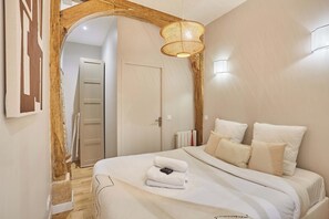 Une chambre avec un grand lit, une arche en bois, un luminaire suspendu et une porte blanche en arrière-plan.