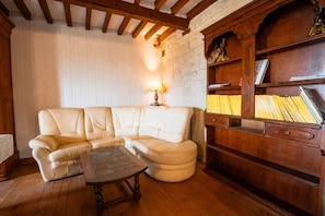Uma sala de estar acolhedora com um sofá de couro branco, uma mesa de centro de madeira e uma estante com livros e objetos decorativos.