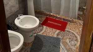 A bathroom with a pedestal sink, a toilet, and a bidet. There is a shower curtain with a bubble pattern, a small window with a view, and a welcome mat. - Bay cabins (Puerto Iguazú)