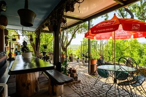 An outdoor patio with tables and chairs, surrounded by potted plants and a view of greenery.