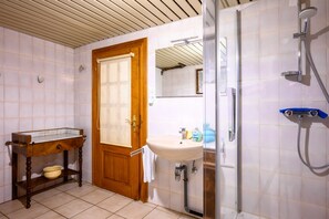 A bathroom with a wooden door, a sink, a mirror, and a shower.