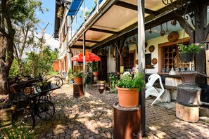 A cobblestone courtyard with a vintage cart, potted plants, and rustic furniture.