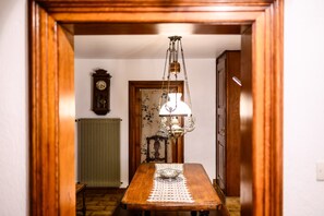 A wooden dining table with a lace tablecloth, a hanging light fixture, a radiator, and a clock on the wall.