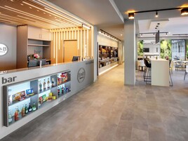 Zona de recepción de un hotel con bar, mostrador de recepción y área de descanso con barra.