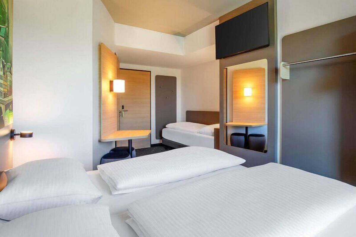 A hotel room with three beds, a flat-screen TV, and a wall-mounted TV.