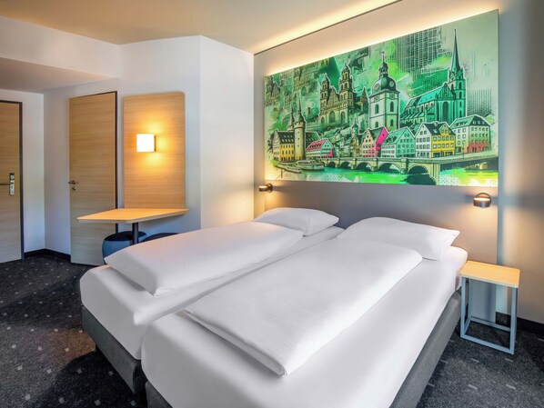 A hotel room with a bed, a nightstand, a wall-mounted lamp, and a painting of a cityscape.