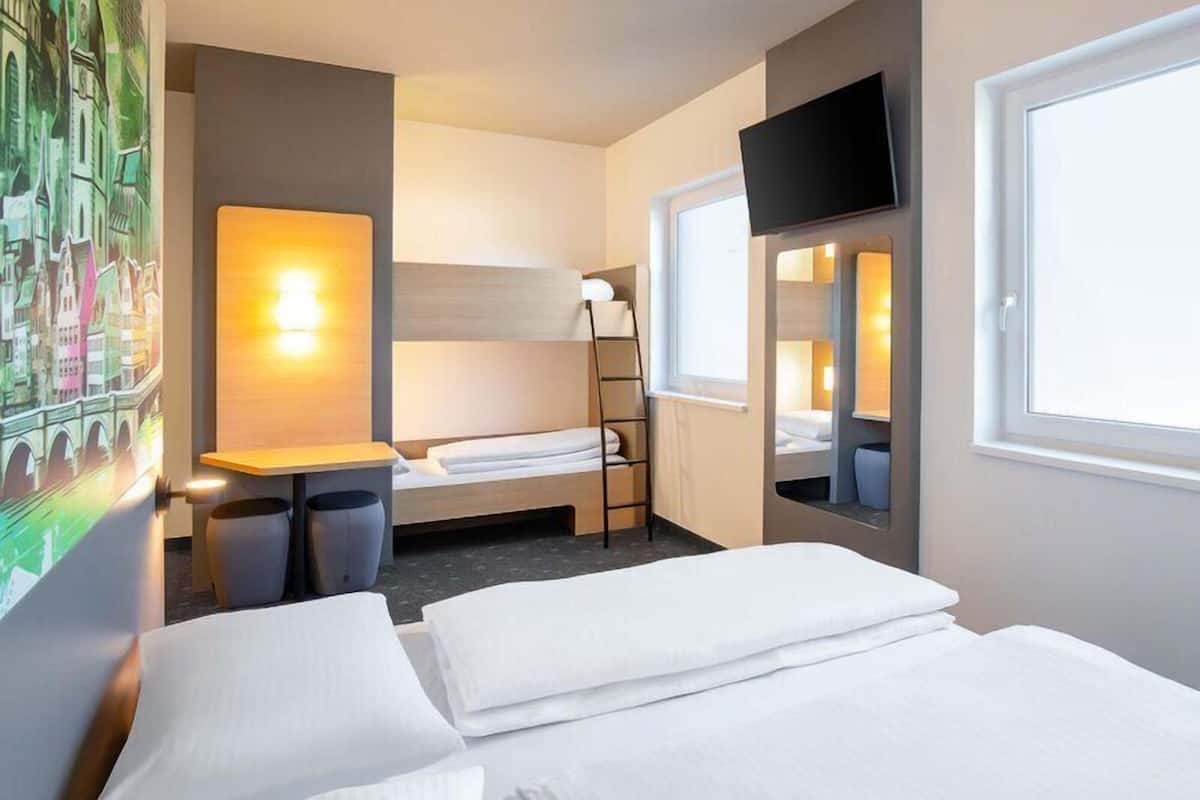 A hotel room with a bed, a desk, a chair, a TV, and a window.