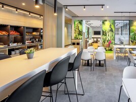 Un lobby de hotel moderno con una zona de bar central, arreglos de asientos y un mural que representa un paisaje urbano.