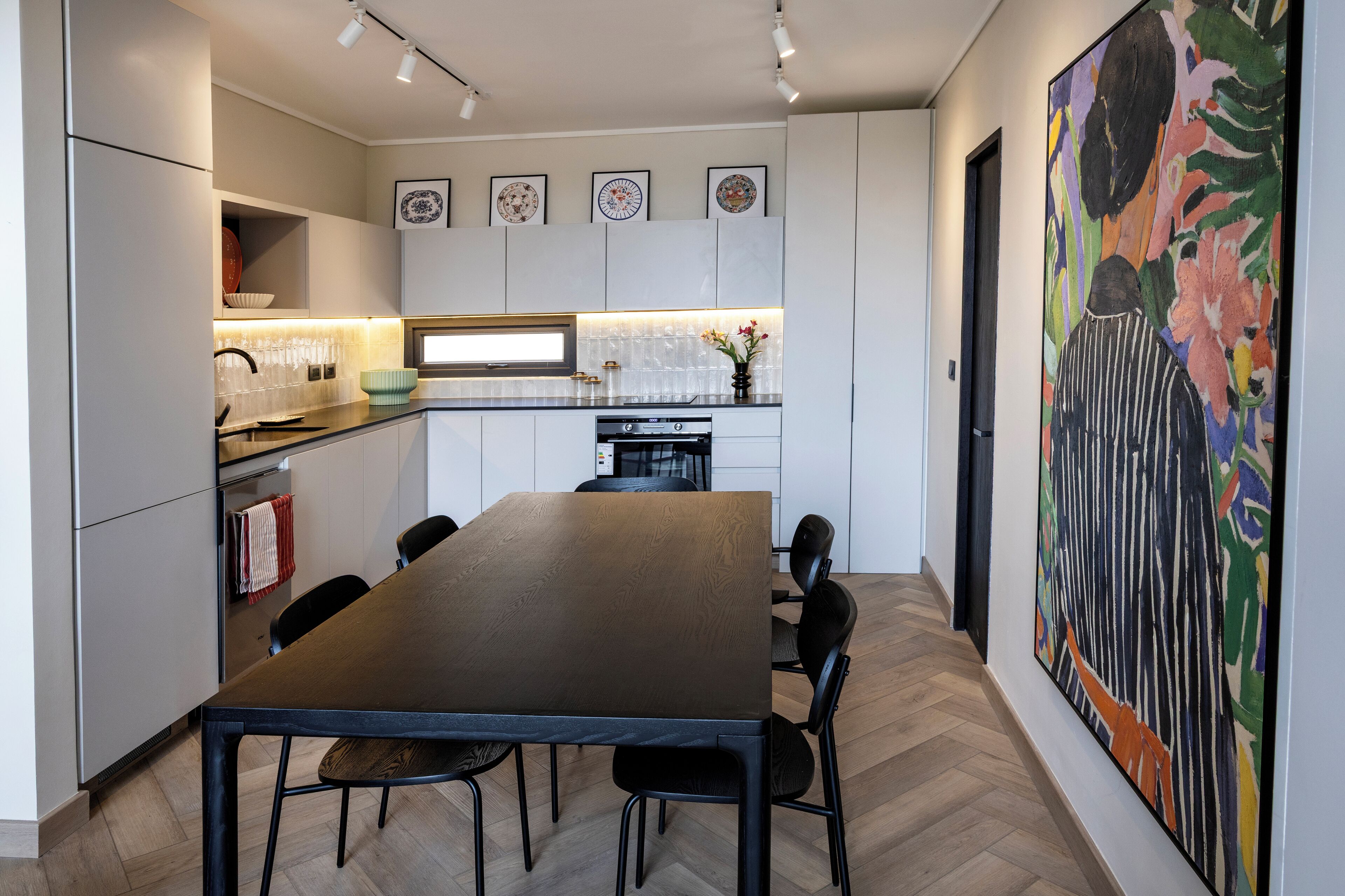 Une cuisine moderne avec une table et des chaises, un réfrigérateur et un grand tableau accroché au mur.