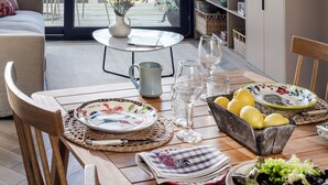 A modern living room with a large window, a dining table set with plates, glasses, and a bowl of lemons. There is a sofa, a chair, and a bookshelf with decorative items. - Pueblo La Dehesa (Lo Barnechea)