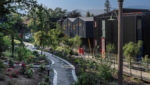 A modern building with a curved pathway, surrounded by greenery and trees. - Pueblo La Dehesa (Lo Barnechea)