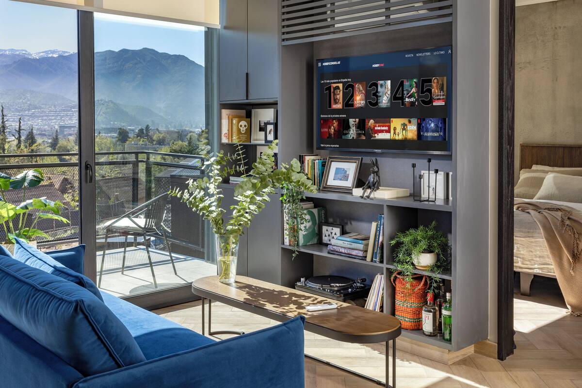 Un salon moderne doté d’une grande fenêtre, d’un canapé bleu, d’une table basse en bois et d’une bibliothèque contenant divers objets.