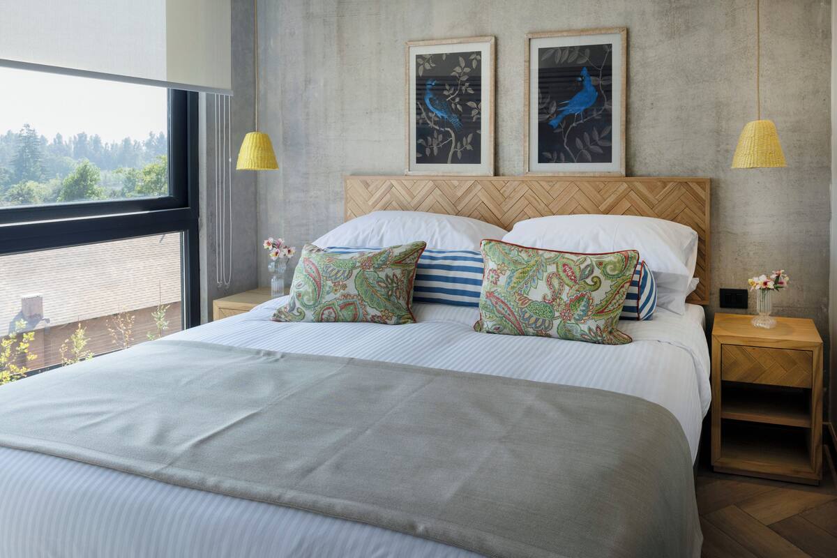 Une chambre avec un grand lit, deux tables de chevet, une fenêtre donnant sur un beau paysage et deux œuvres d’art encadrées accrochées au mur.