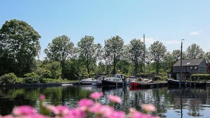 A calm water body with boats docked, surrounded by trees and a house. - Suny bungalow with a private jetty. (Lemmer)
