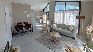 A modern living room with a sofa, coffee table, dining area, and kitchen in the background. - Suny bungalow with a private jetty. (Lemmer)