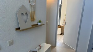 A hallway with a white wall, a wooden shelf with a plant, a decorative wall hanging, and a white console table with a basket. - Suny bungalow with a private jetty. (Lemmer)
