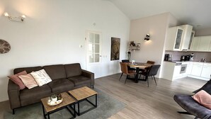 Ein modernes Wohnzimmer mit einem braunen Sofa, einem Couchtisch und einem Essbereich mit Tisch und Stühlen.