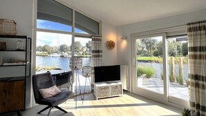 Ein modernes Wohnzimmer mit großem Fenster, einem Flachbildfernseher, einem schwarzen Sessel und einem kleinen Tisch.