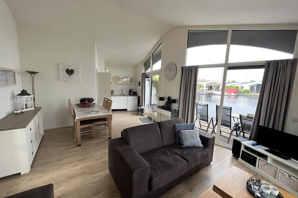 A modern living room with a brown sofa, a dining table, and a kitchen in the background.