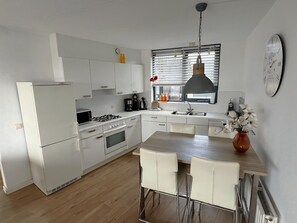 Une cuisine moderne avec des meubles blancs, une cuisinière à gaz, un évier et un coin repas comprenant une table et des chaises en bois.