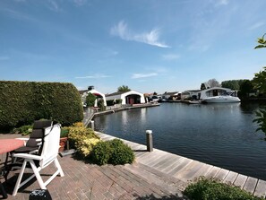 Ein Flussufer mit einem Boot, einer Holzterrasse und einem kleinen Tisch mit Stühlen.