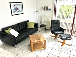 Un salon moderne avec un canapé noir, une table basse en bois, un fauteuil en cuir noir et un radiateur.