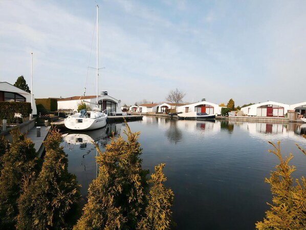 Un port de plaisance où un voilier est amarré, entouré de bâtiments modernes dotés de grandes fenêtres, et dont la surface d’eau, calme, reflète les structures environnantes.