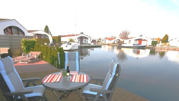 Terraza con dos sillas y una mesa, con vista a un cuerpo de agua tranquilo y barcos.