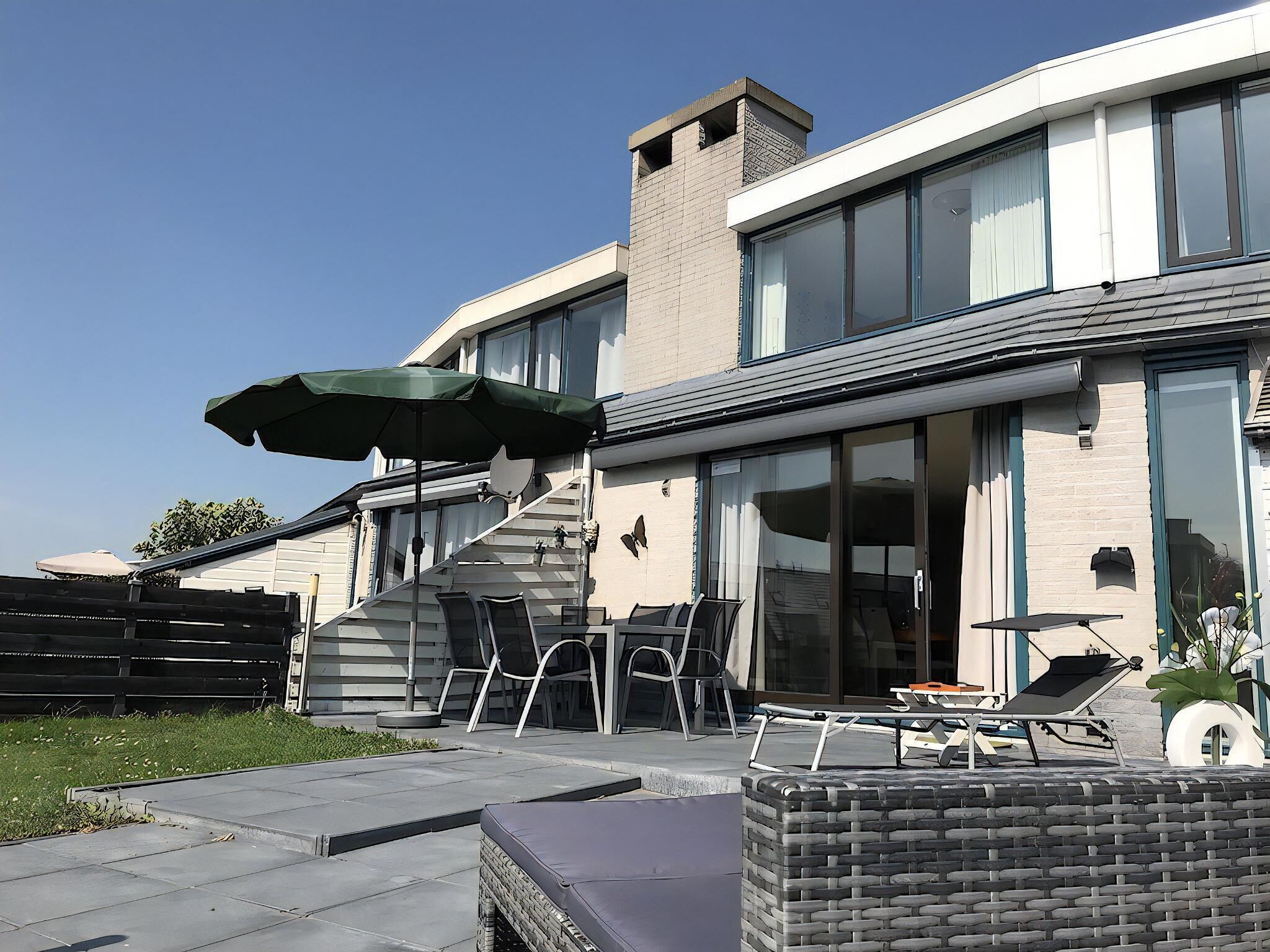 Una casa moderna con patio, mobiliario exterior y una sombrilla grande.